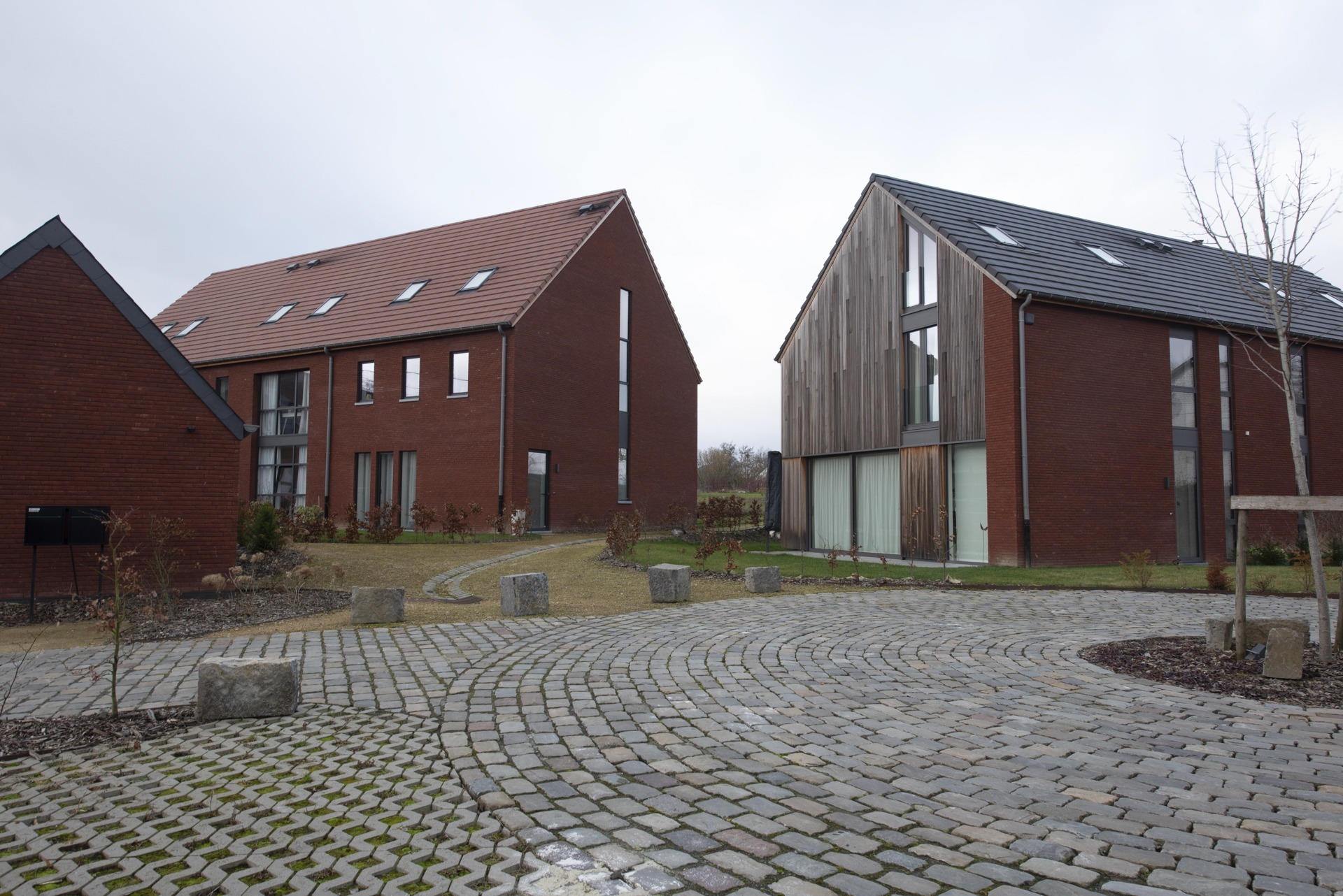 Une maison d'architecte en brique rouge avec une allée et une maison avec un bardage en bois